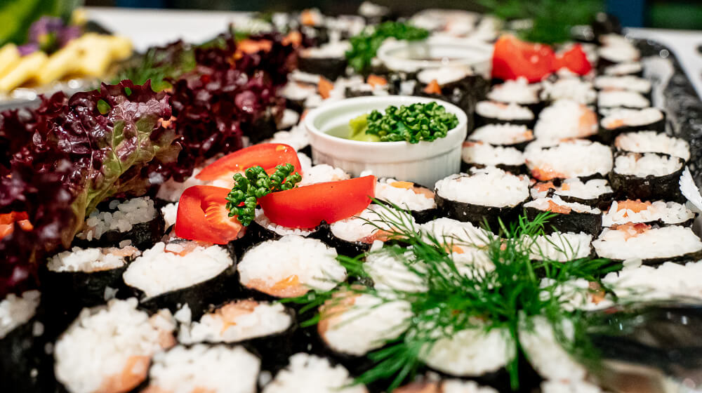 Sushiröllchen liegen mit Tomaten und Dill verziert auf einer Platte auf einem Buffet
