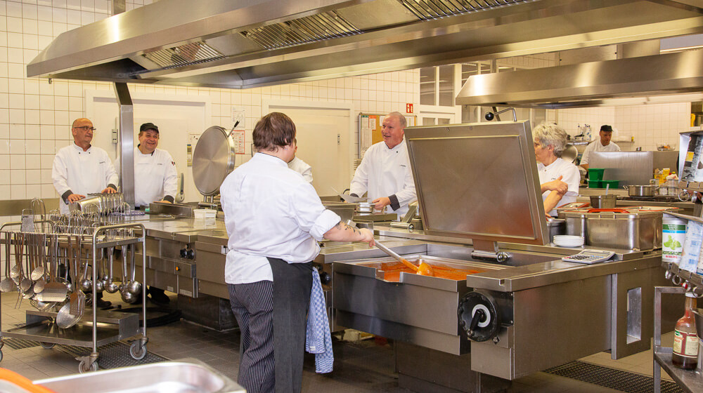In einer Großküche sind verschiedene Köche und Helfer bei der Zubereitung von Speisen