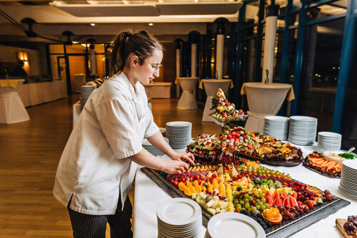 Eine Mitarbeiterin richtet ein Obstbuffet mit verschiedenen Obstsorten