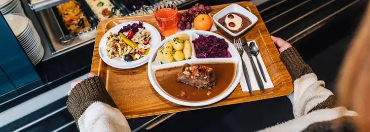 Eine Person trägt ein Tablett mit verschiedenen Speisen