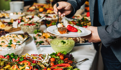 Eine Person bedient sich an einem Buffet mit vielen verschiedenen Speisen