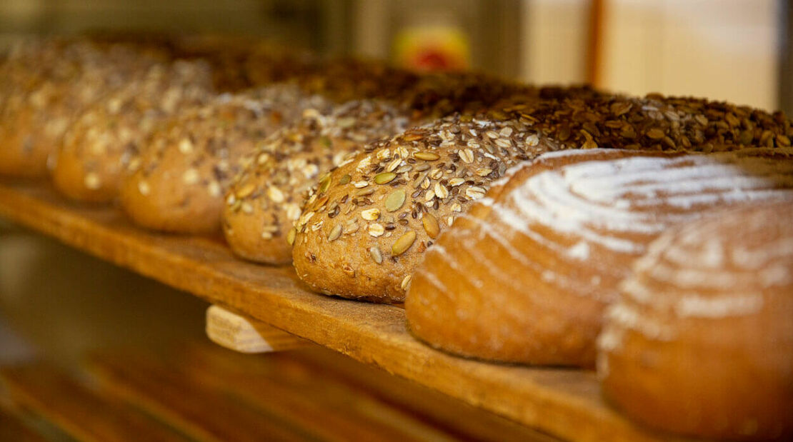 Frisch gebackene Brote liegen in einem Holzregal nebeinander.