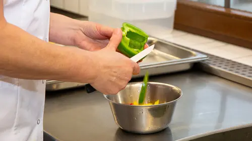 Eine Paprika wird mit einem Messer in Scheiben geschnitten