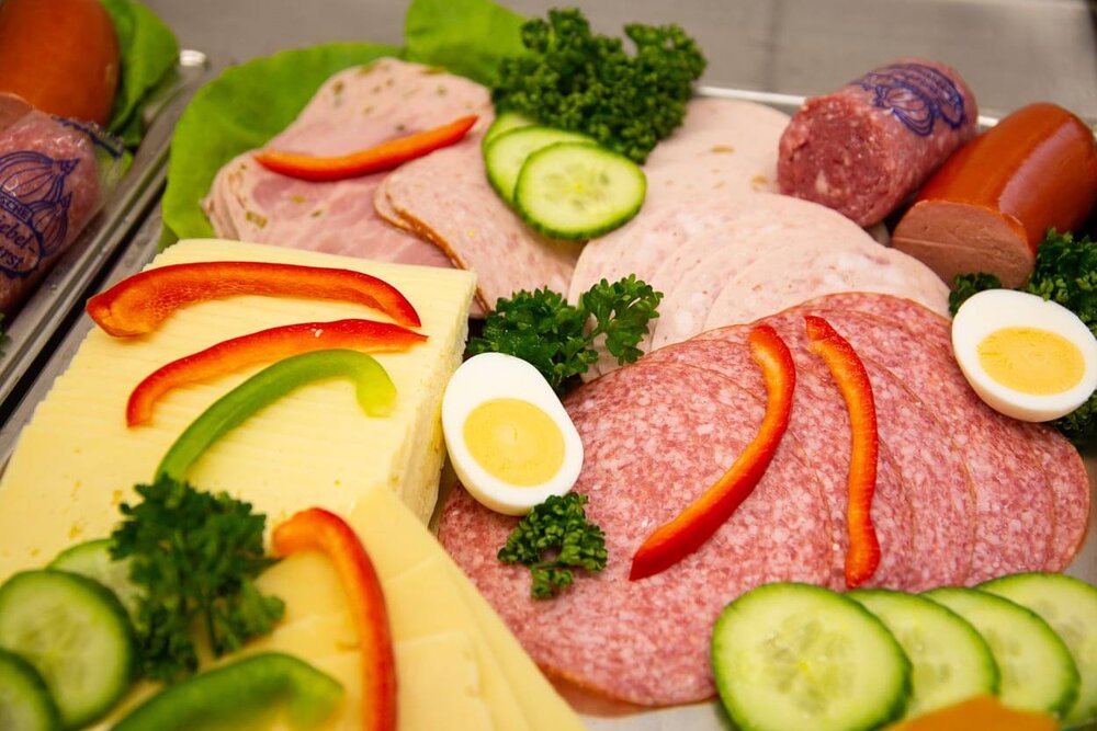 Geschnittene Käse- und Wurstscheiben liegen mit Eiern, Paprika und Gurken garniert auf einer Platte