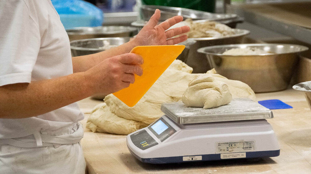 Ein Mitarbeiter hat eine Formhilfe in der Hand, um Teig zu formen