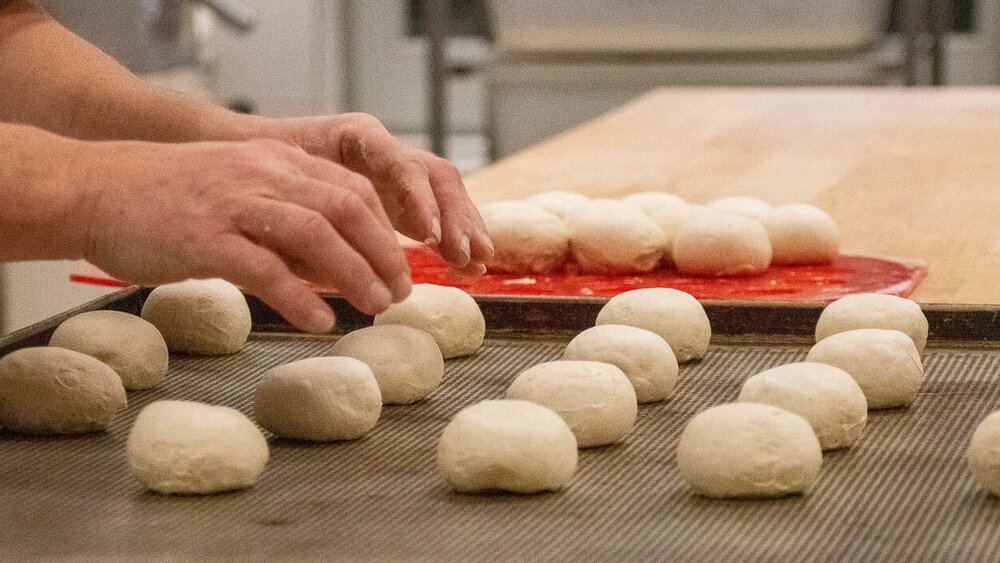 Ungebackene Brötchen werden frisch auf ein Backblech nebeneinander gelegt
