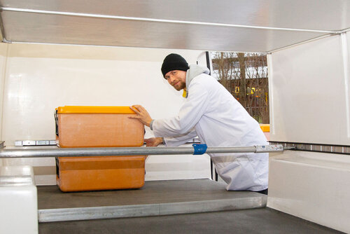 Ein Mann schiebt eine Isolierbox in einen leeren Laderaum eines Transporters